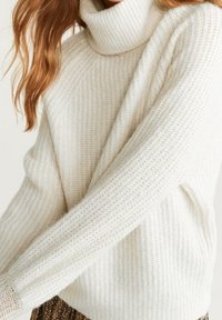 Crème-kleurige coltrui met een textuurpatroon, lange mouwen en een relaxte pasvorm. Zacht materiaal met ribbelaccenten.