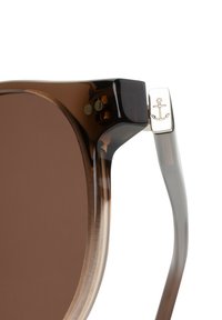 Schildpatt-Sonnenbrille mit braunen Gläsern, klaren Rahmenkanten und silbernem Ankerdetail an den Bügeln. Glatte Oberfläche, modernes Design.