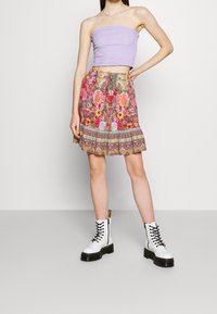 Haut lavande sans bretelles avec une texture froncée ; jupe florale colorée avec un ourlet à volants ; associée à des bottes de combat blanches à lacets.
