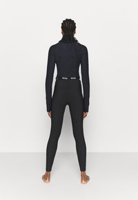Maglietta nera a maniche lunghe e leggings aderenti, entrambi realizzati in tessuto elasticizzato. I leggings hanno un cinturino con logo e una texture liscia.