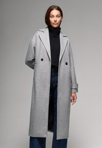 Szary wełniany płaszcz w mieszance materiałów o długim kroju, z klapami w stylu notch, podwójnymi guzikami i szerokimi rękawami, nałożony na czarny golf.