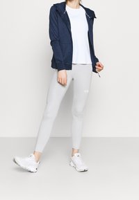 Mörkblå huva-jacka med diamantmönster, vit t-shirt, ljusgrå leggings och vita träningsskor. Texturerat material, åtsittande silhuett.