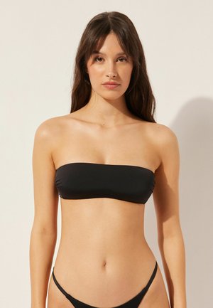 Schwarzes Bandeau-Bikini-Oberteil mit Raffung, nahtlosem Design und weichem Stoff. Kombiniert mit minimalistischen schwarzen Bikiniunterteilen.
