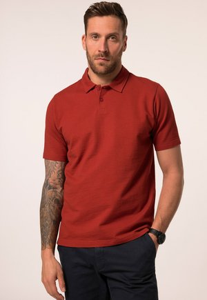 Polo rouge avec un motif texturé, à manches courtes et col à trois boutons. Porté avec un pantalon noir et une montre noire au poignet.