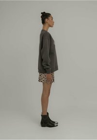 Sweatshirt oversize gris, shorts à imprimé léopard, bottines noires avec un embout en métal argenté, présentés sur un fond neutre.