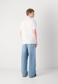 Hvit kortermet polo skjorte kombinert med løse lyseblå jeans, med et enkelt design og en avslappet silhuett. Svarte sko fullfører antrekket.