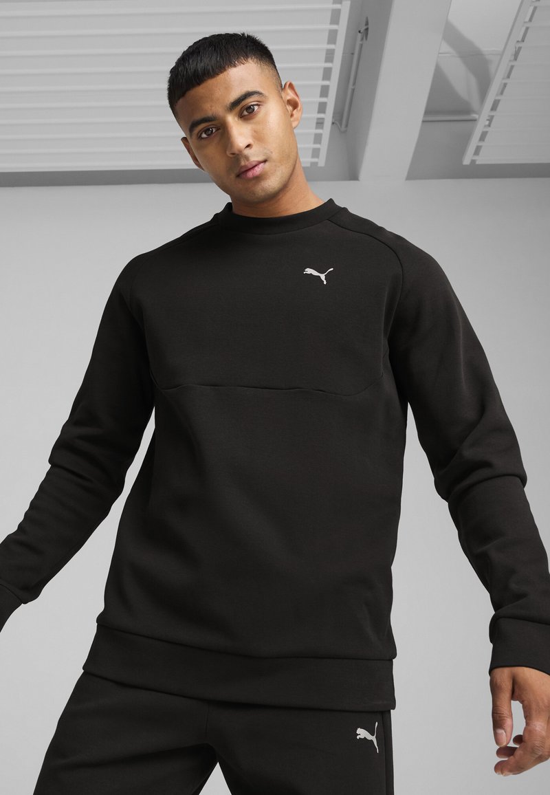 Sweat-shirt noir à manches longues, col rond et poignets côtelés. Présente un panneau horizontal et un petit logo blanc sur la poitrine. Tissu doux.