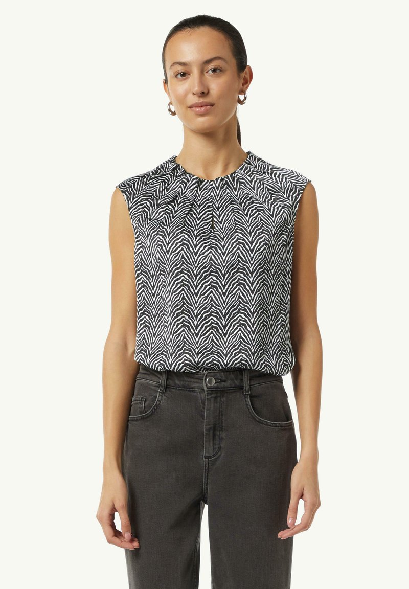 Schwarzes und weißes ärmelloses Top mit Zebra-Streifenmuster, kombiniert mit dunkelgrauen, hoch taillierten Jeans, die eine lässige Silhouette betonen.