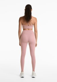 Lichtroze sportbh met kruisbanden, gecombineerd met hoog-gewijde, strakke roze legging en witte sportschoenen. Gladstoftextuur.