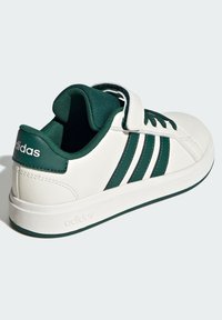 White and dark green Adidas sneaker with three stripes, Velcro strap, padded collar, and branded heel and sole details.