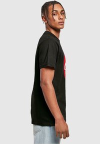 Sort kortærmet T-shirt med et fremtrædende rødt rundt logo på fronten. T-shirten har en afslappet pasform og en blød bomuldsstruktur.