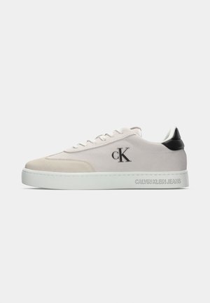 Low-top beige sneaker with white sole, black heel tab, "cK" logo on side, and "Calvin Klein Jeans" embossed on midsole.