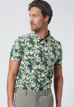 Camisa verde de manga corta con un patrón de hojas crema, cuello abotonado y corte slim. Combinada con pantalones grises, que presentan una cinturilla estándar.