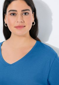 Blaues V-Ausschnitt-T-Shirt aus weichem Stoff, mit kurzen Ärmeln und glatter Oberfläche. Silberne Creolen runden den Look ab.