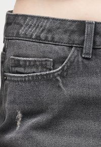 Κοντινό πλάνο της μέσης και της μπροστινής τσέπης γκρι τζιν, με ορατό θηλάκι για ζώνη και μικρή φθορά κάτω από την τσέπη.