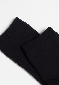 Calcetines de algodón negro con una textura suave, que presentan un puño acanalado y un diseño sencillo, dispuestos en plano sobre un fondo blanco.