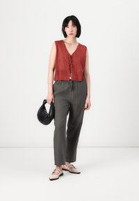 Top de punto corto en color óxido con escote en V y lazo en el frente, combinado con pantalones gris oscuro de cintura elástica. La modelo sostiene un bolso negro.