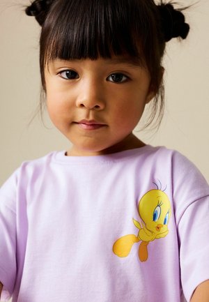 Lilac t-shirt featuring a yellow cartoon character with blue eyes and feather details. Short sleeves and soft, smooth fabric texture.
