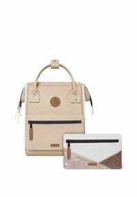 Beige stoffen rugzak met een handvat en rits, met een rond logo patch en een kleinere witte en beige ritszak met geometrisch ontwerp.