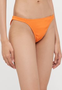 Narancssárga bordázott bikini alsó, keskeny oldalszíjakkal és minimális fedettséggel. Sima textúra és rugalmas derékpánt a kényelemért.