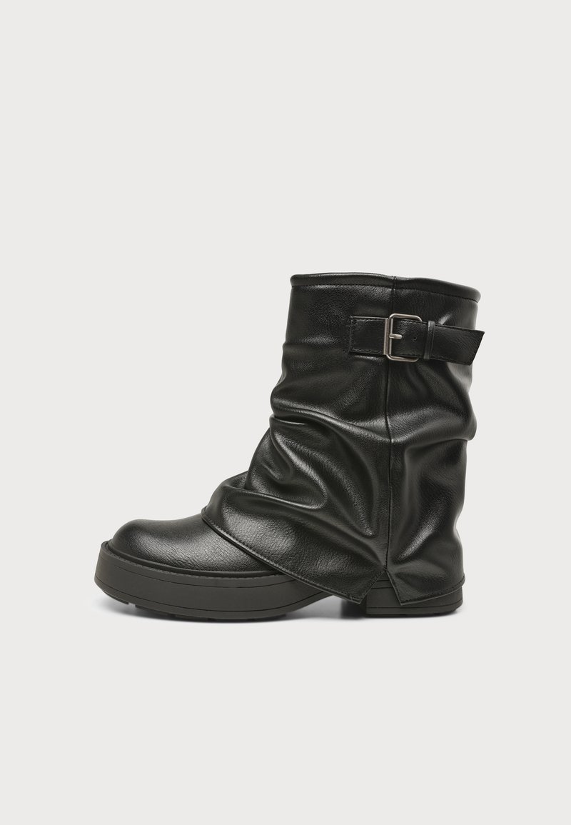 Botte en cuir noire mi-mollet avec un design froissé, bout rond, semelle plate et bride de boucle réglable près du haut.