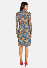 Blaues Blumenkleid mit langen Ärmeln, einer figuresschmeichelnden Silhouette und einem knielangen Saum. Verziert mit leuchtend orangefarbenen und roten Blumen.