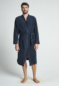Accappatoio blu navy in morbido tessuto, con dettagli in piping rosso, maniche lunghe, due tasche frontali e vita con cintura.
