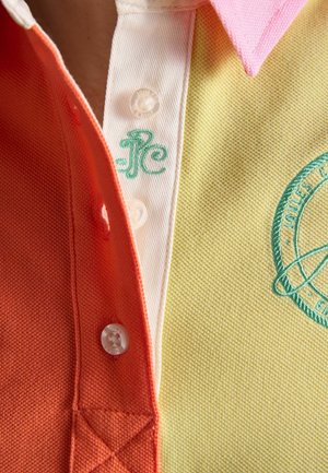 Prim-plan al unui tricou polo multicolor cu secțiuni portocalii, albe și galbene, prezentând nasturi și logo-uri brodate verzi.