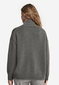 Grauer gestrickter Pullover mit hohem Kragen, übergroßem Design, geripptem Saum und langen Ärmeln. Die Textur wirkt weich und dicht.