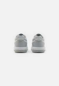 Šedé kožené sportovní boty s bílou podrážkou, s logem "New Balance" na patě, hladkým povrchem a nízkým designem.
