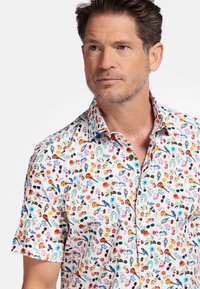 Chemise à manches courtes avec un fond blanc et un imprimé floral et d'objets multicolore. Col décontracté et boutons marron.