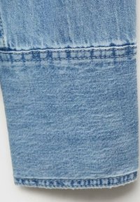 Hellblauer Denim-Stoff mit einer leicht verwaschenen Textur, der am unteren Rand mit einem doppelt genähten Saumdetail versehen ist.