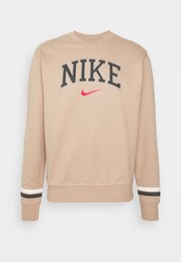 Nike beige sweatshirt med grå text "NIKE," rosa swoosh-logotyp, ribbad rundhals och randiga detaljer i svart och vitt vid muddar.