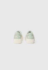 Green canvas sneakers with embroidered daisies on the heels, white rubber soles, and a ribbed texture at the sole's edge.