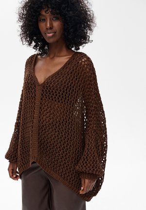 Brązowy sweter robiony na drutach o luźnym, otwartym kroju, z dekoltem w serek i długimi rękawami. Teksturalny splot dodaje wizualnego zainteresowania i głębi.