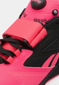 Reebok športová obuv s jasne ružovým zvrškom, čiernymi akcentmi, textúrovaným pásikom, kontrastnými šnúrkami a systémom pumpy na nastavenie prispôsobenia.