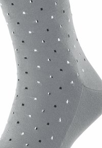 Graue Socken mit einem strukturierten Strickdesign und verstreuten schwarz-weißen Punkten. Knöchelhöhe mit einem glatten, dehnbaren Abschluss.