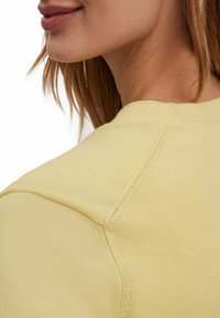Lichtgele gebreide sweater met een ronde halslijn, geribbelde schoudernaad en een gladde textuur. Minimalistisch ontwerp zonder zichtbare patronen.