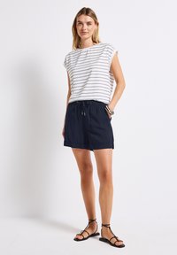 Randig vit och marinblå topp med korta ärmar, matched med marinblå shorts med elastisk midja och dragsko, kompletterat med svarta sandaler.