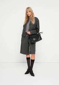 Giacca di pelle grigia sopra un maglione texturizzato, abbinata a pantaloni corti grigi. Borsa nera con un design arricciato, stivali neri con tacco e calze fino al ginocchio.