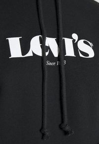 Hoodie nero con logo Levi's bianco e la dicitura "Dal 1853" sottostante, che mostra un primo piano del tessuto e dei lacci neri.