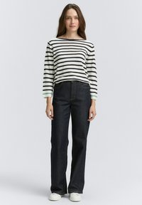 Gestreepte lange mouwen shirt in crème en zwart met groene accenten; gecombineerd met donkerblauwe wijde jeans. Witte sneakers maken de look compleet.