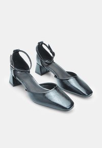 Black faux leather block-heeled shoes with a square toe and ankle strap. Features a smooth texture and minimal design.