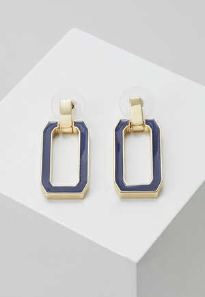 Prostokątne kolczyki wiszące w złotym odcieniu z granatową emalią, prezentowane na białej pochylonej powierzchni.
