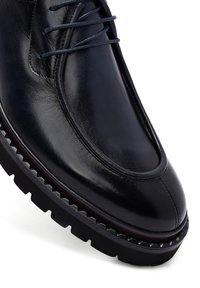 Zwarte leren schoen met een gladde afwerking, voorzien van een ronde neus, een contrasterende rubberen zool met gekartelde randen en donkere veters.