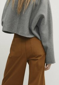Grijze, korte trui van zachte gebreide stof, gecombineerd met bruine wijde broek met twee achterzakken en een gladde textuur.