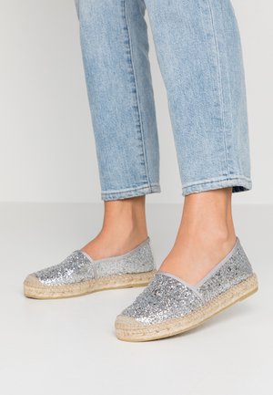 Espadrilles argentées scintillantes avec des semelles en jute tressé, bout rond et côtés élastiqués, associées à un jean bleu clair.