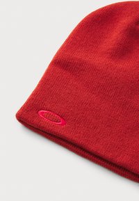 Red knit beanie made from soft fabric, featuring a close-fitting design and a small embroidered logo in contrasting pink.