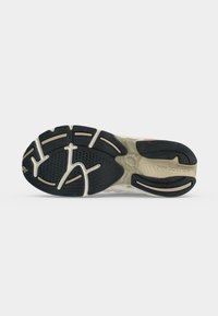 Σόλα παπουτσιού New Balance με μαύρο πέλμα και μπεζ ενδιάμεση σόλα, που δείχνει υφή λαβής και το κείμενο "new balance" στην περιοχή της φτέρνας.