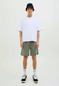 T-shirt oversize blanche, short vert olive, chapeau seau noir, baskets noir et blanc, chaussettes blanches. Ensemble de vêtements de fitness décontracté.